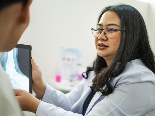 Caregiver holds an x-ray while talking with a patient.