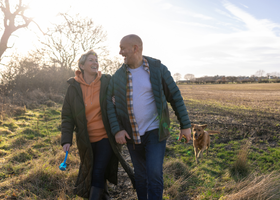 A couple walking across a field with their dog.