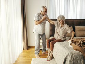 An older man helps his wife out of bed