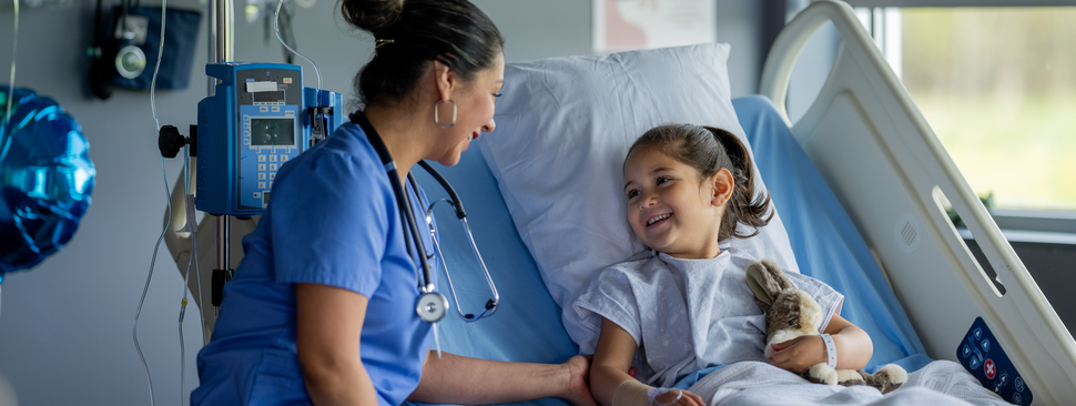 Provider sits with young patient smiling while in hospital bed.