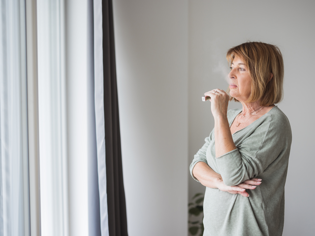 Mature woman standing by the window and smoking an electronic cigarette