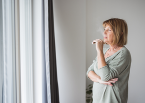 An older woman smokes from a vape while looking out of her window