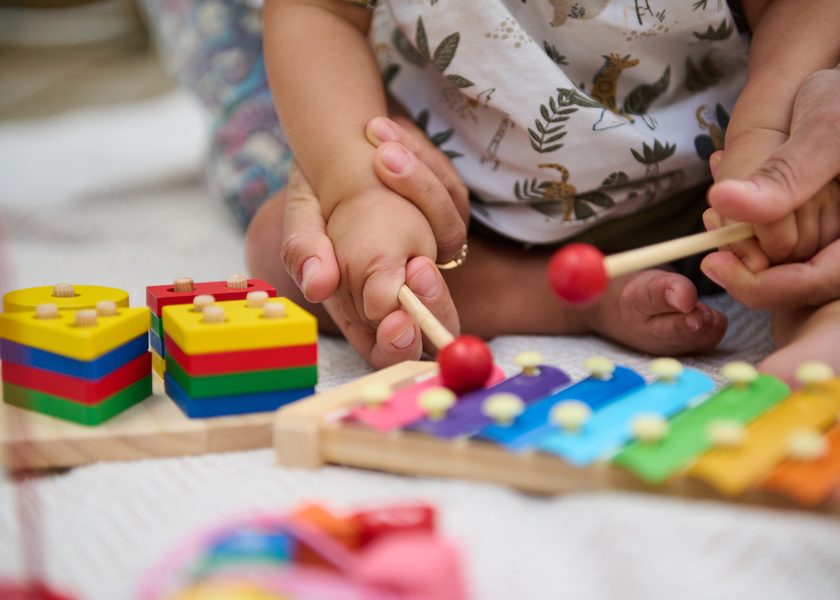 Adult holding baby's hands playing xylophone