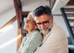 A man hugs his wife from behind while in their living room