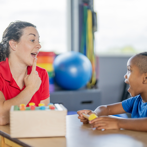 A woman in a red shirt pointing to her chin showing a child something 