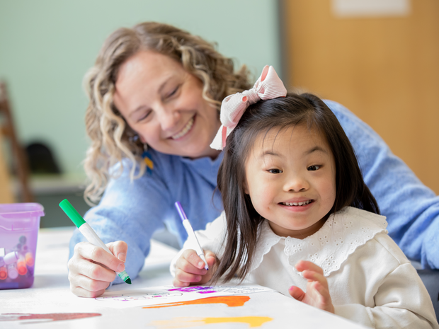 young girl with down syndrome is being helped by a middle aged woman