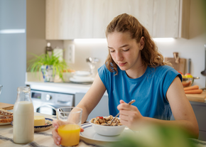 A teenager sits at the table while eating breakfast