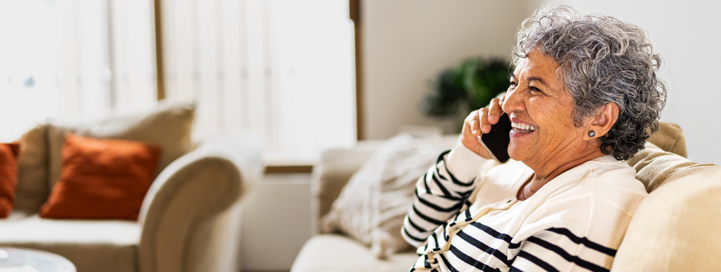 A woman sits on the couch, talking on her cell phone
