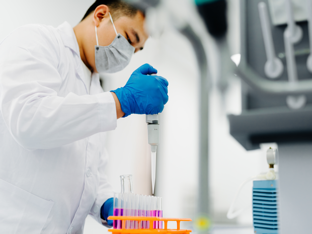 Male clinical researcher in mask puts sample into holder.