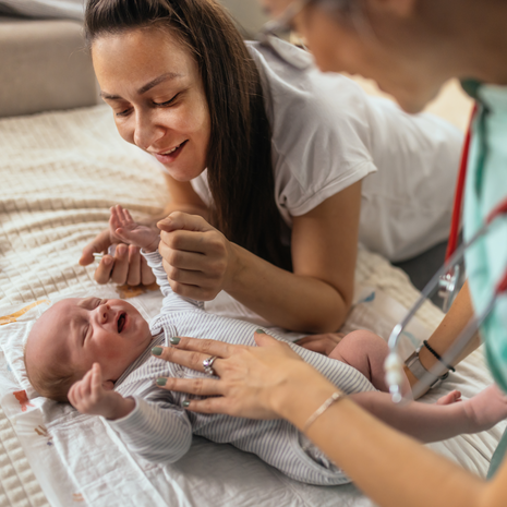 Female doctor at house visit, checking up newborn baby