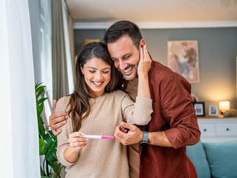 A couple looks at a pregnancy test with surprised smiles on their faces