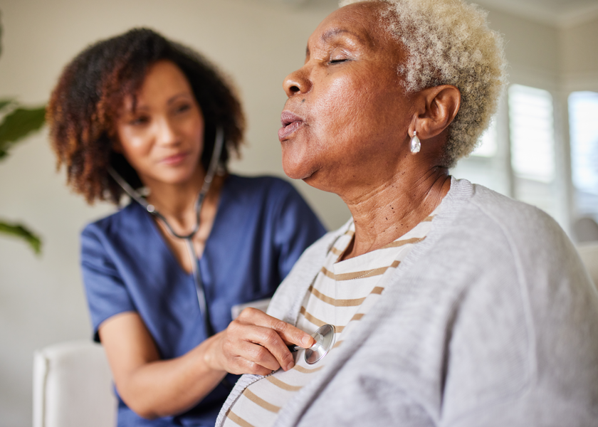 An older woman closes her eyes as a nurse checks her heart rate