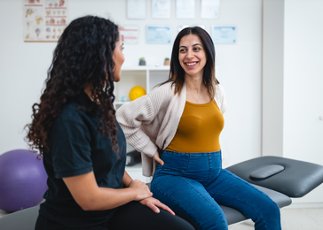 A pregnant woman holds her back while speaking with a physical therapist