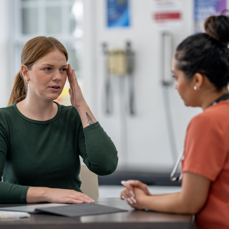 A young woman meets with her female doctor as she discusses her recent migraines.
