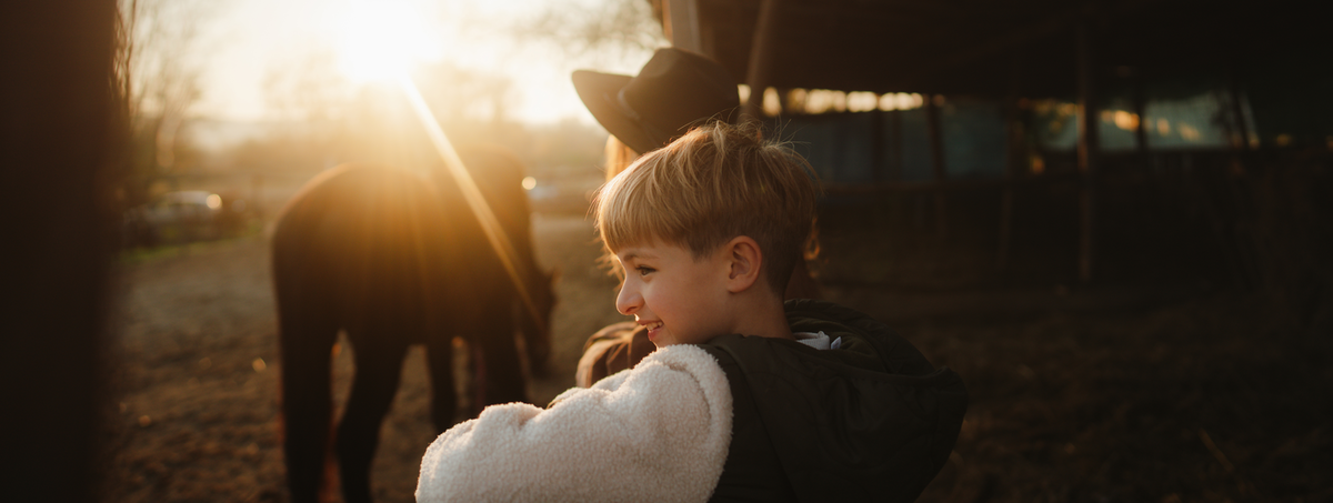 A boy watches his horse while the sun is rising.