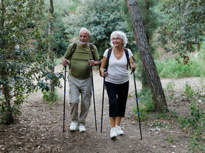 Happy senior couple hiking in the woods using trekking poles