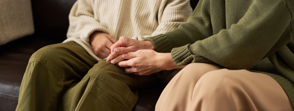 Older couple hold hands on couch.