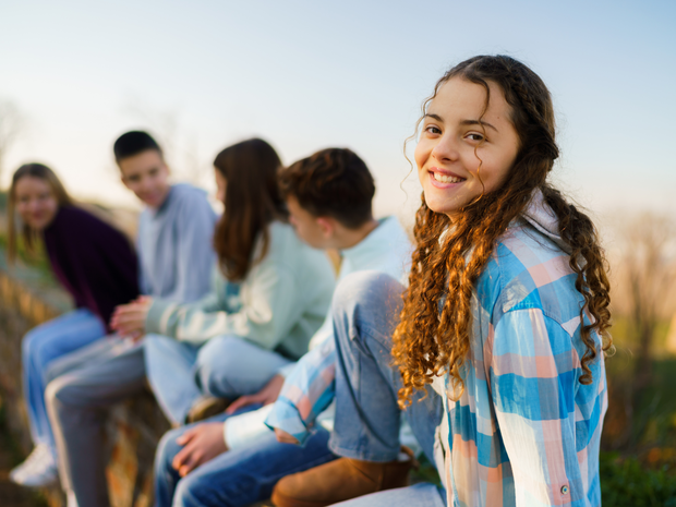 Happy teenage girl sitting on a wall with her friends outdoors
