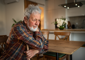 Older man sits at table with arms crossed.