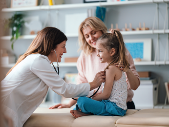Provider smiles while checking young girl's heart rate with her stethoscope.