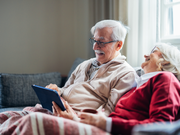 Elderly couple laugh while sitting on couch.