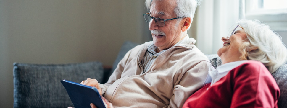 Couple sitting on the couch pointing at a electronic tablet.