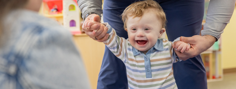 Young boy with Down syndrome taking first steps with help from his parents