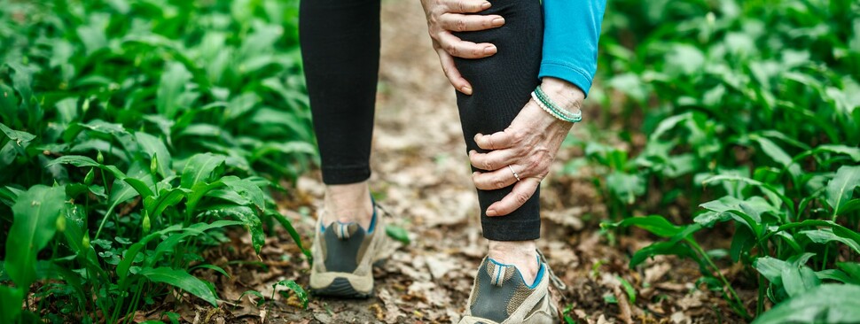 Woman suffering from leg pain during a run in a forest 