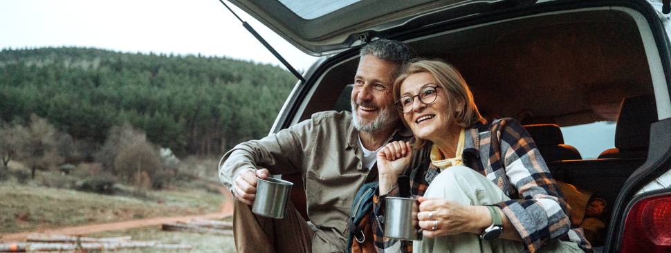 Happy couple sitting outside in the back of their car drinking coffee 