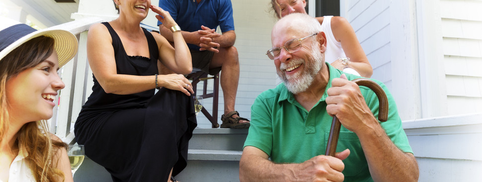 A man with a cane laughs on the front porch with his family