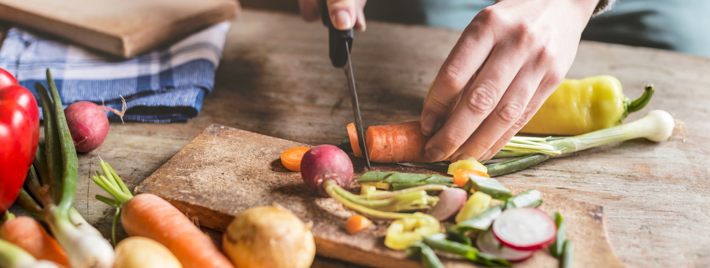 Hands cut a carrot, with various other vegetables scattered around