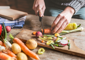 Hands cut vegetables on a wooden cutting board