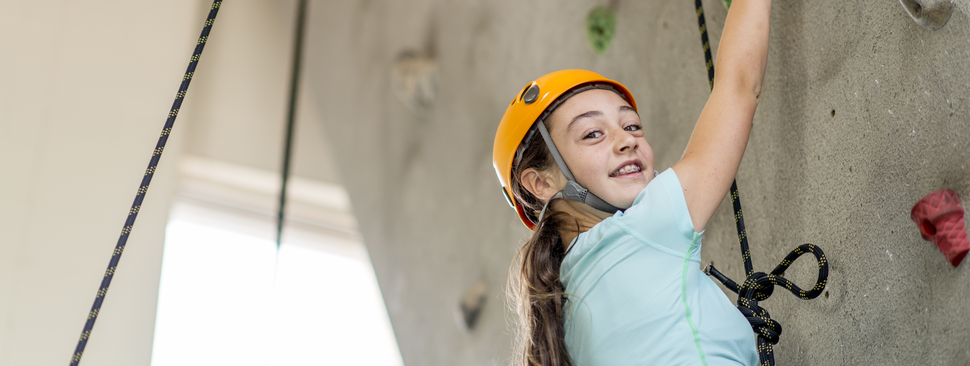 A girl looks out as she hangs onto a rock climbing wall