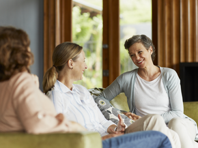 A trio of women sit on a sofa as they chat