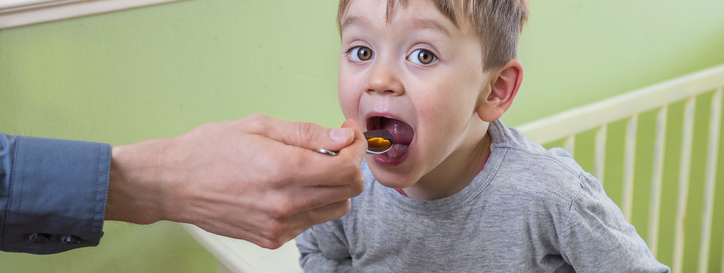 A young boy takes cough medicine