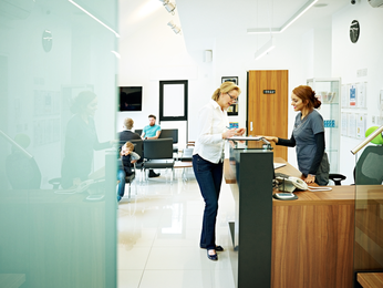 Woman provider hands clipboard to patient at desk.