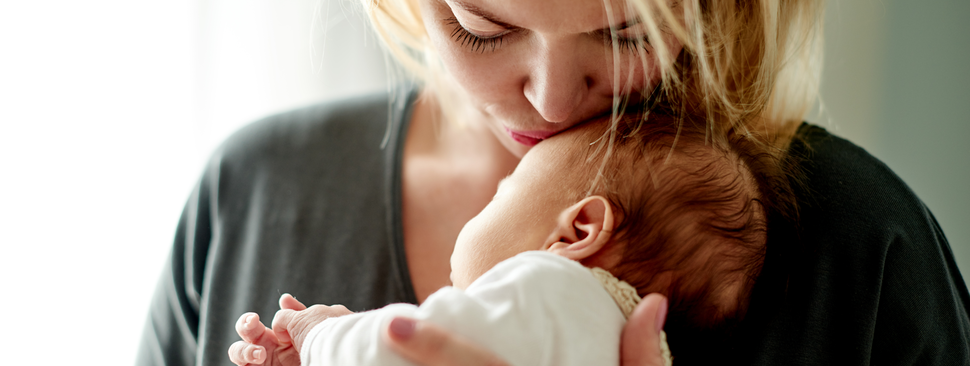 Mother kissing newborn baby boy head while putting her child to sleep