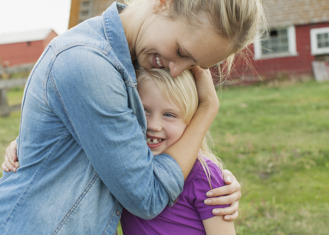 A woman leans down to hug a smiling girl