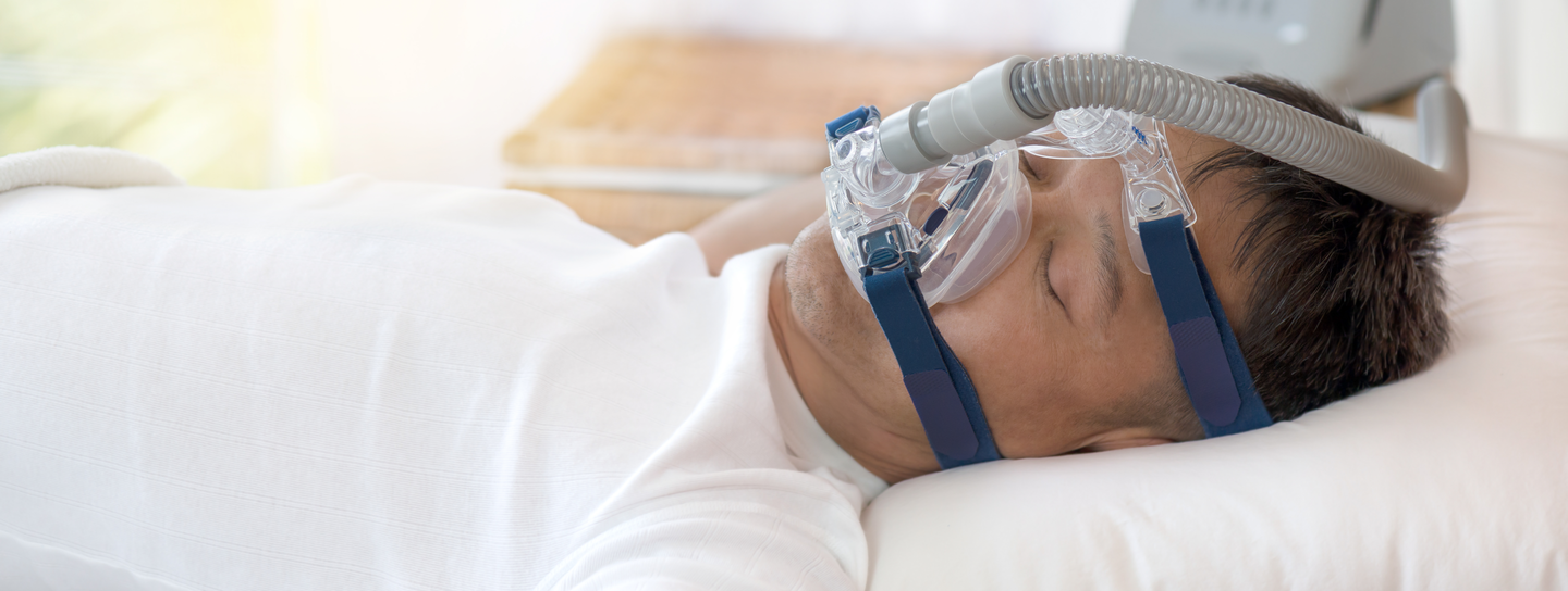 A man lays on his back in bed, wearing a Continuous Positive Airway Pressure (CPAP) device