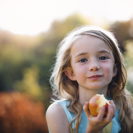 A girl eats an apple while outside.