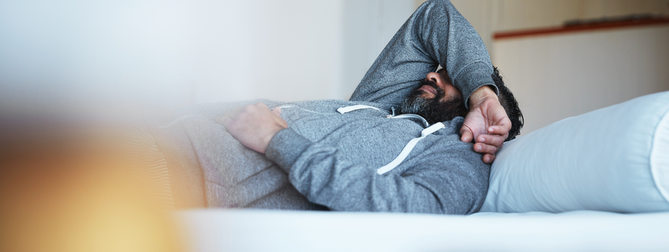 A man lays on a bed with an arm covering his eyes