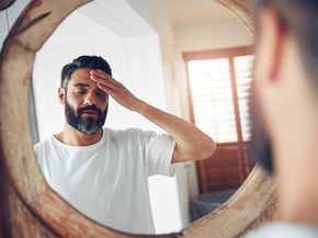 Man looks in mirror and rubs forehead in pain