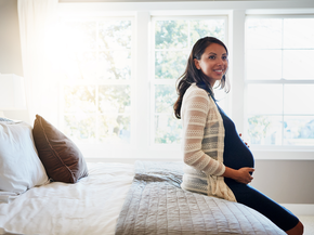 Pregnant mother sitting on end of bed smiling