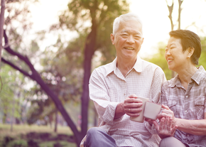 A woman and her husband clink their cups while seated outdoors