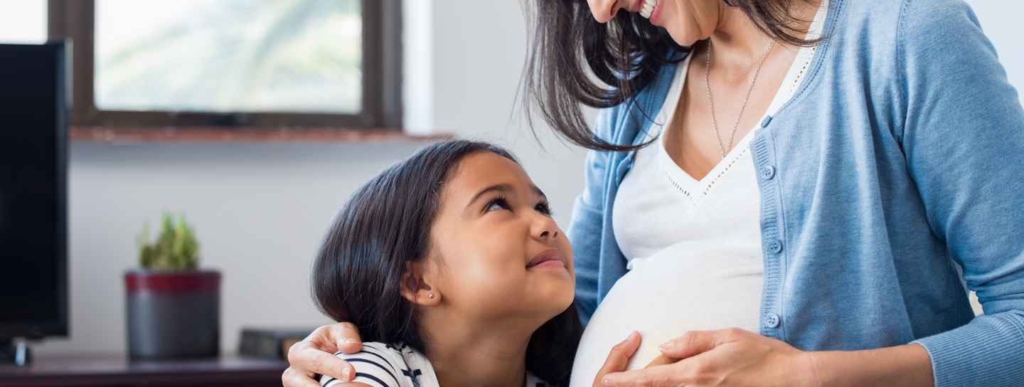 A daughter holder her hand over her mom's pregnant belly.