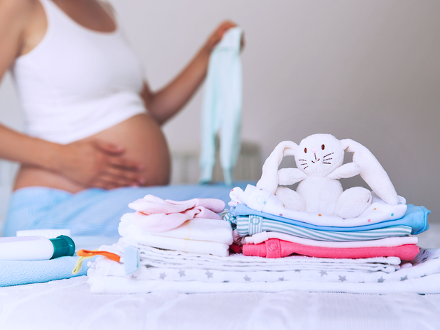 Baby toys stacked on a bed with mother in the background