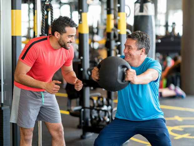 man exercising with kettlebells and the support of a trainer