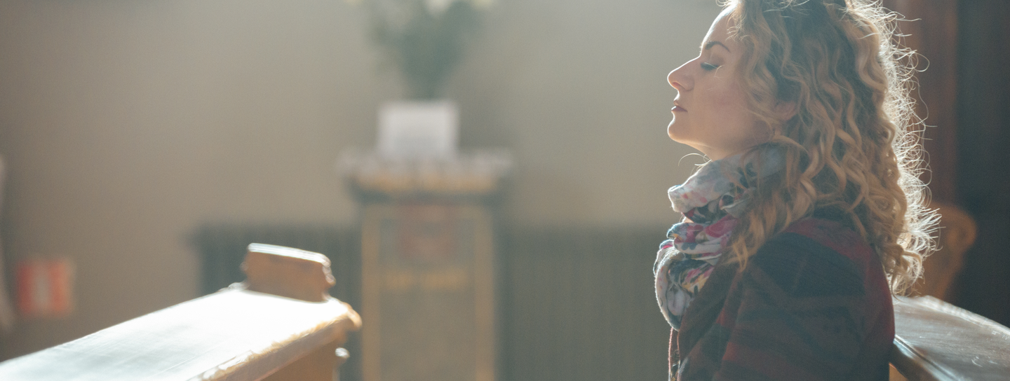 Woman with eyes closed sitting in a church.