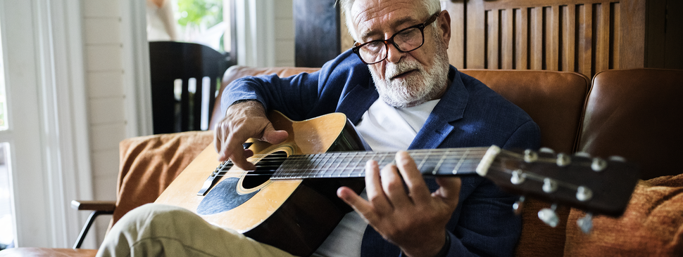 An older man sits on a couch, playing guitar