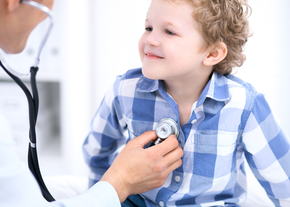 A young boy smiles as a doctor checks his heart